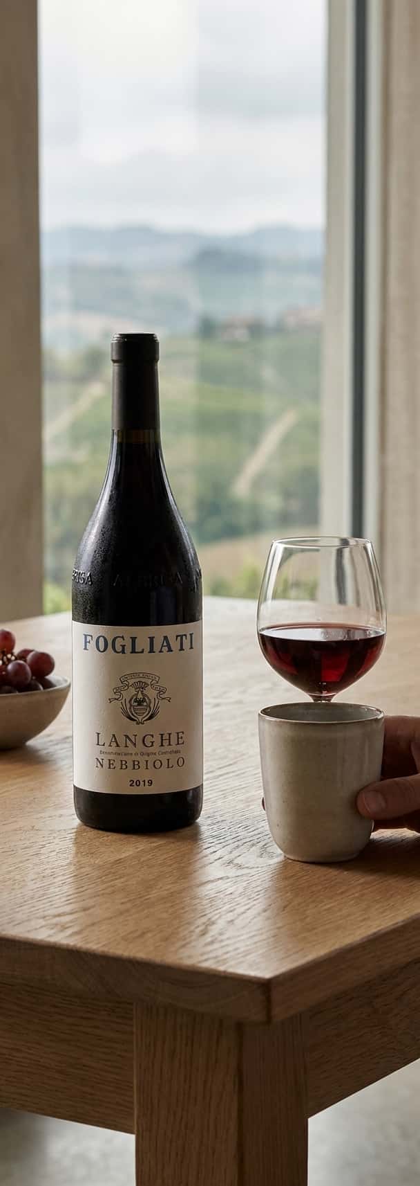 Bottle of Fogliati Langhe Nebbiolo 2022 against a backdrop of Piedmont's hills and vineyards