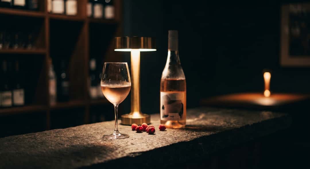 Suuri piknikori vihreällä nurmikolla kesäauringossa, etualalla rosé-viiniä, hedelmiä ja laseja