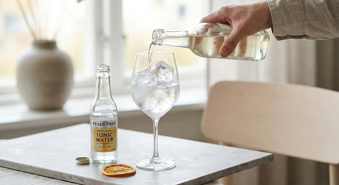 Nærbilde av hvit portvin som helles over is i et stort glass, med tonic-flaske og appelsinskive ved siden av