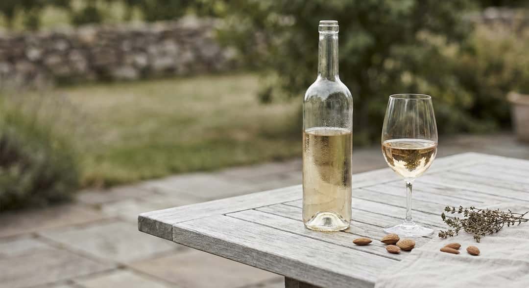 A bottle of white Rioja on a wooden outdoor table, green garden in the background, natural daylight