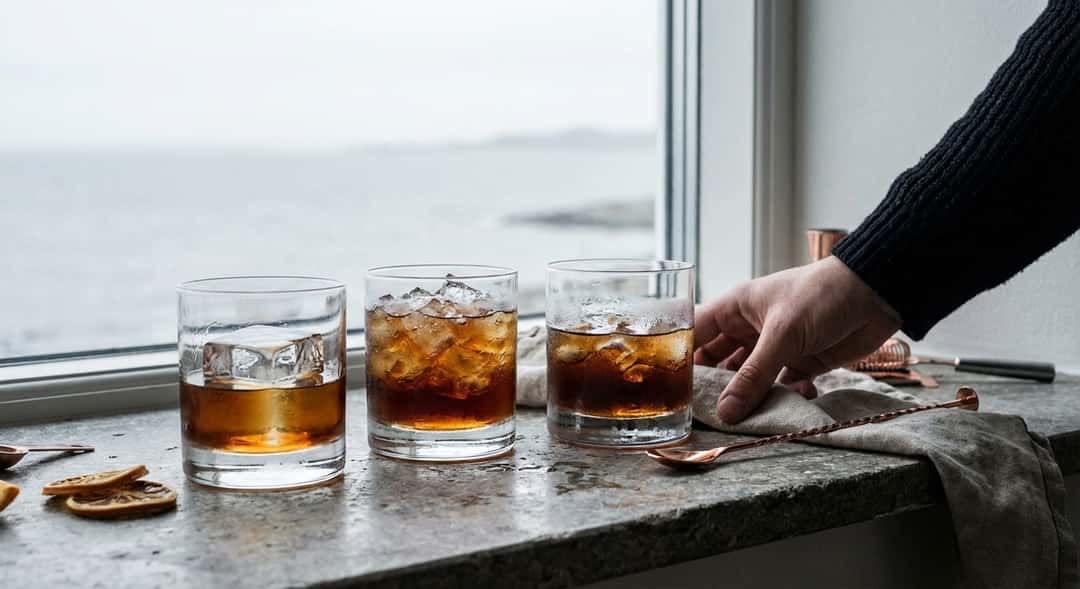 Nærbilde av tre glass side ved side – ett med stor klar isbit, ett med knust is, ett med små isbiter – alle med mørk væs