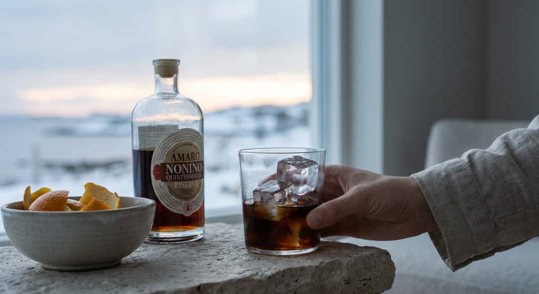 Three different amaro bottles on a rustic wooden table, sunset in the background, large ice cubes in glasses (Averna Amaro Siciliano)
