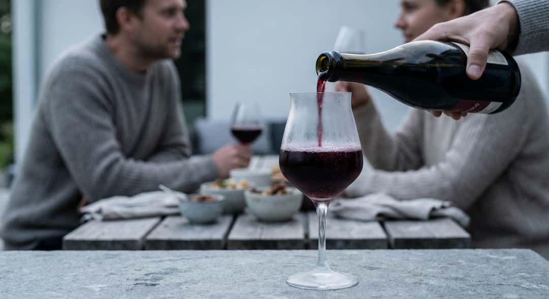 Käsi kaataa Lambrusco-viiniä viileään lasiin, kuplat nousevat selvästi, rento kesäilta ulkona