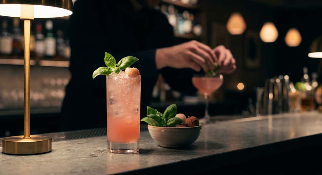 A frosted highball glass filled with lychee spritz, crushed ice, rosé, and fresh basil in a summery outdoor setting with greenery
