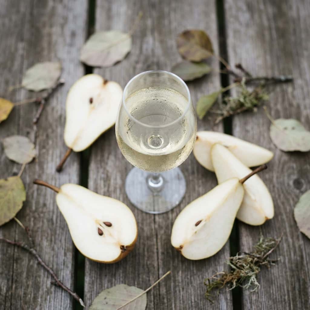 Närbild av uppskurna päron i höstligt ljus på en trädbänk, bredvid ett glas vitvin