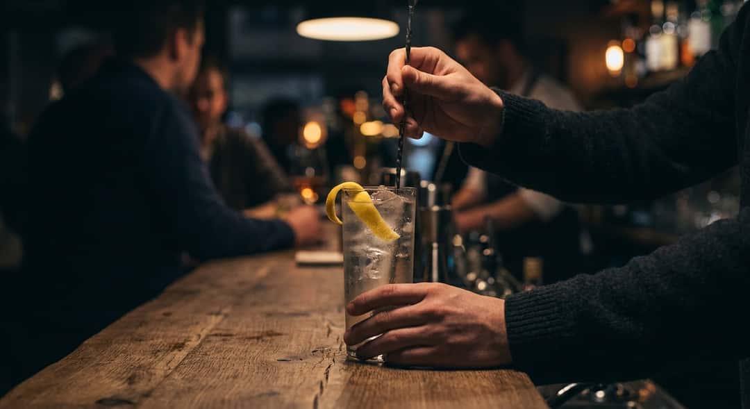 En iskald highball i et langt glass med brus og sake, garnert med sitronskall, servert på en trebenk i sommerkveldslys