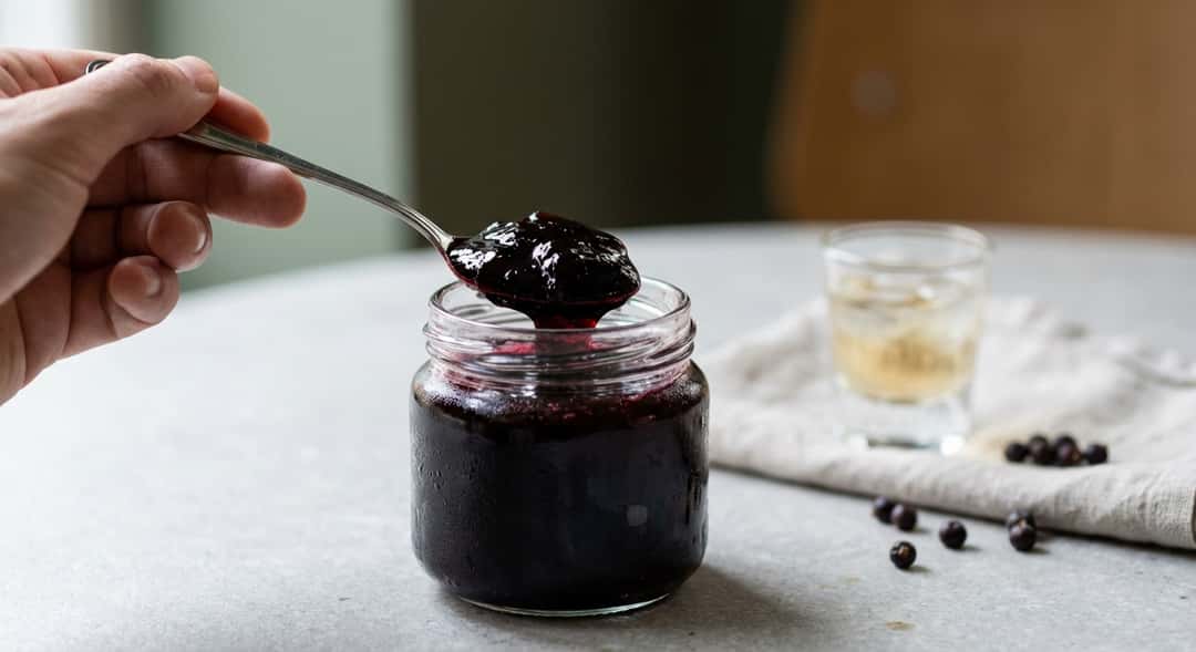 Close-up of a spoon lifting dark blackcurrant jelly from a jar, texture and sheen visible