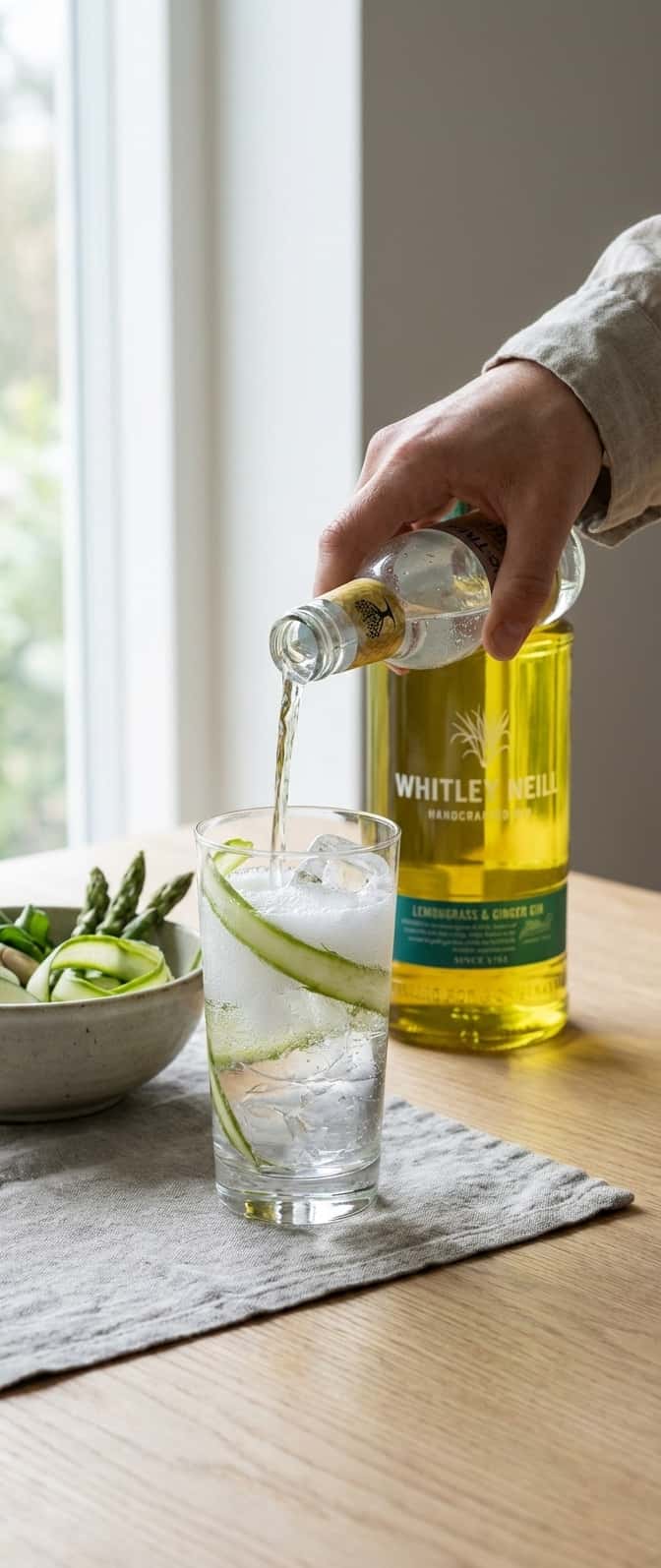 Høyt glass med aspargesstrimler synlige i isen, tonic helles fra flaske, (Whitley Neill Lemongrass & Ginger)
