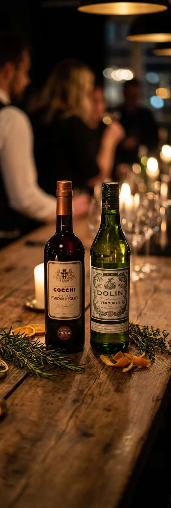 Två flaskor vermouth sida vid sida – Cocchi Vermouth di Torino och Dolin Dry – på en träbordsskiva med örter och apelsinskal