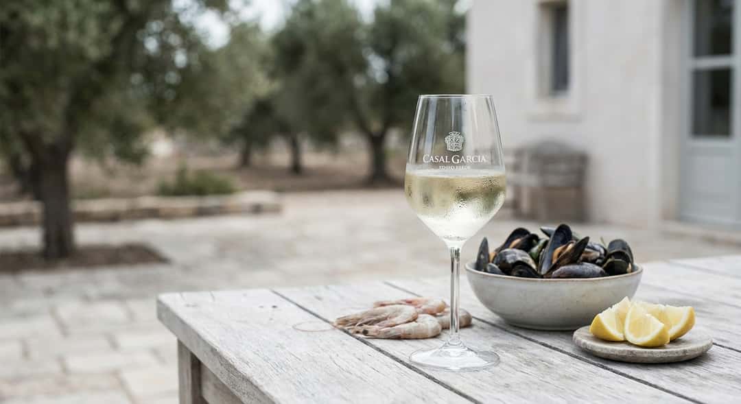 Ett kallt glas Vinho Verde med lätt imma på utsidan, serverat bredvid färsk skaldjur och citronklyftor på ett utomhusbord i trä
